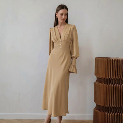 Elegant warm beige midi dress with a romantic V-neck, voluminous bishop sleeves, and pearl button details, shown on a model from the waist up against a studio background.