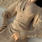 Elegant beige chiffon midi dress featuring a romantic V-neckline, voluminous bishop sleeves with pearl button cuffs, and a fitted waist. Shown on a model resting against a textured sandy background.