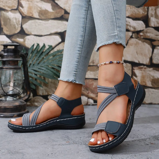 Zykla women's dark blue comfort sport sandals with criss-cross elastic straps and beige accents, shown on a model wearing light-wash jeans.