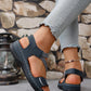 Dark blue and beige women's comfort sport sandals with white stitching shown on a model's feet, featuring criss-cross elastic straps and faux leather accents, worn with light-wash jeans.