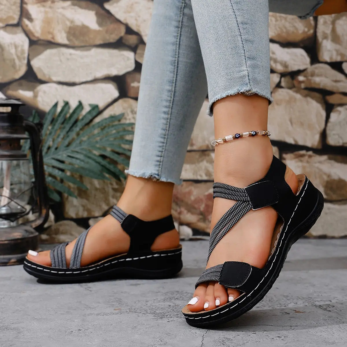 Zykla women's comfort sport sandals in black with criss-cross elastic straps and beige accents, worn with light-wash denim jeans.