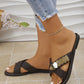 Dark brown Zylae embellished cross-strap flat sandals worn with distressed denim jeans, showcasing the unique gold, silver, and rose gold metal embellishment and white contrast stitching.