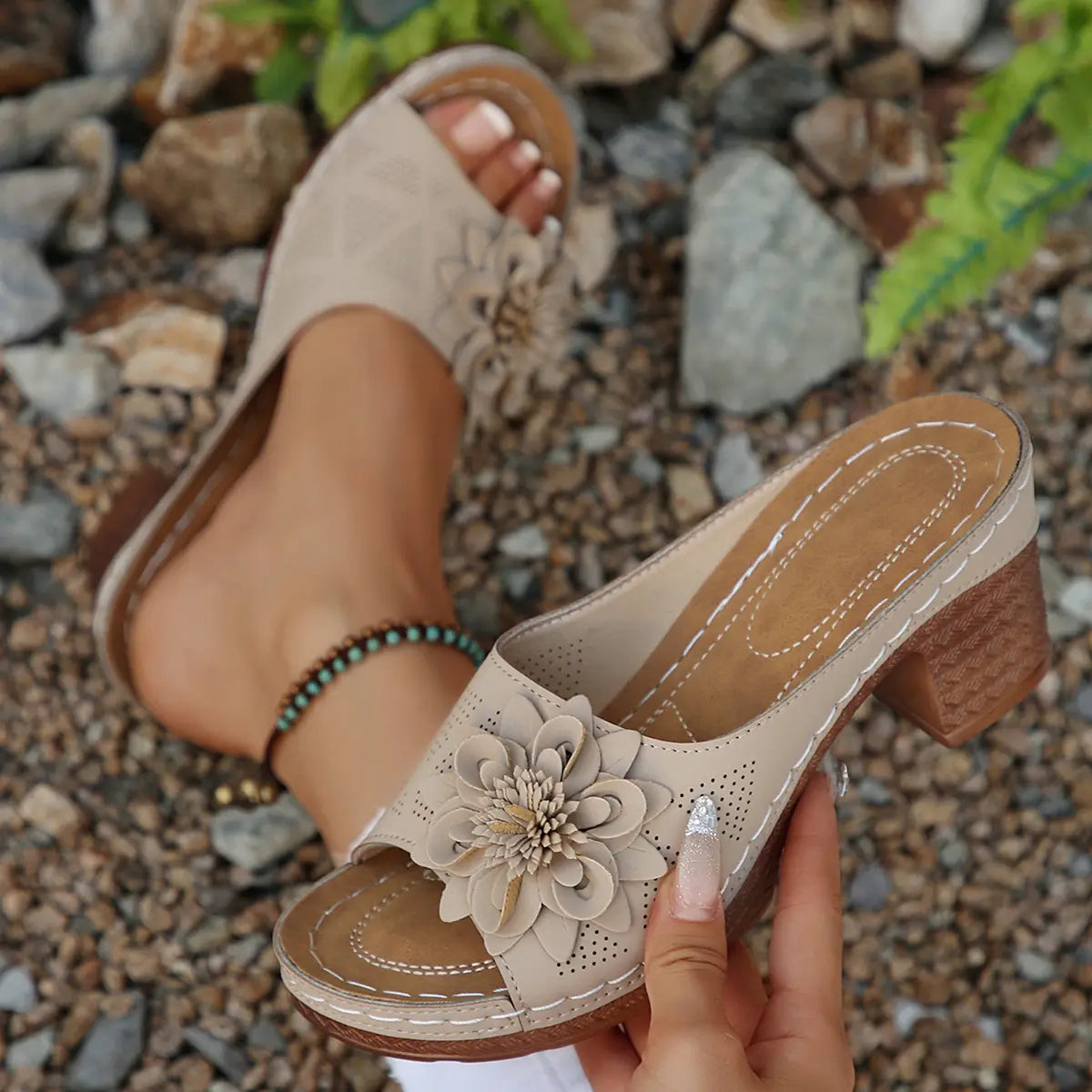 Beige Zylaya wedge sandals with a peep-toe design, featuring a delicate layered floral applique and perforated straps, shown outdoors on gravel.