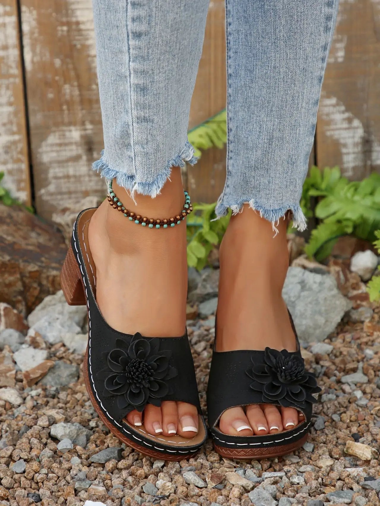Black Zylaya women's wedge sandals featuring a layered floral applique, perforated strap, peep-toe, and a chunky 4cm wood-effect heel, shown on feet with distressed denim jeans.