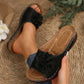 Black Zylia women's slip-on sandals adorned with layered fabric floral embellishments and perforated straps, shown on feet in a relaxed, casual setting.