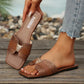 Brown square-toe flat slide sandals featuring a snakeskin-embossed strap adorned with a gold-tone leopard head embellishment, styled on a foot with denim jeans.