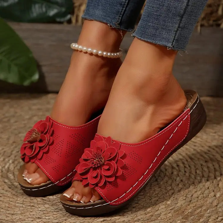 Red Zylia women's open-toe slip-on sandals featuring a large, layered floral embellishment and perforated faux leather straps, worn with denim jeans and a pearl anklet.