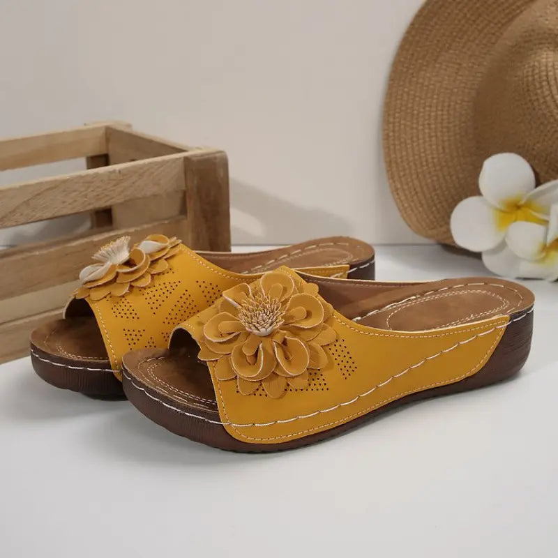 Zylia yellow floral embellished slide sandals with perforated straps and low wedge soles, styled with a straw hat and decorative flower.