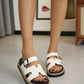 Woman wearing white Zylo platform slide sandals with a distinctive H-strap design, featuring an adjustable gunmetal buckle and a layered sole with white contrast stitching.