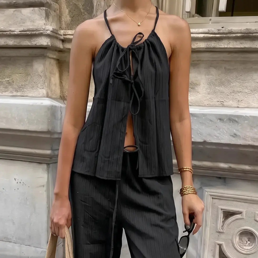 A woman models the Zyloria black bohemian linen set, showcasing a halter neck top with adjustable tie and flowy wide-leg pants, accessorized with a tote bag and sunglasses in an urban outdoor setting.