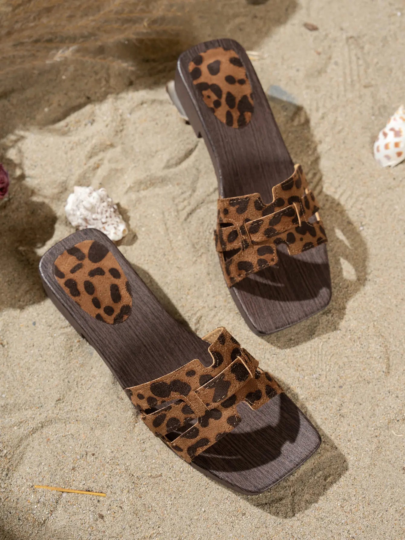 Zyloria chic summer flat slide sandals in leopard print with layered faux suede straps and a dark wood-effect stacked heel, resting on a sandy beach with shells.