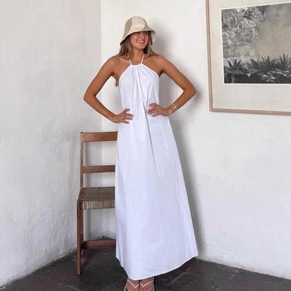 Zyloria white halter maxi dress with open back and A-line silhouette, worn by a model in a resort setting.