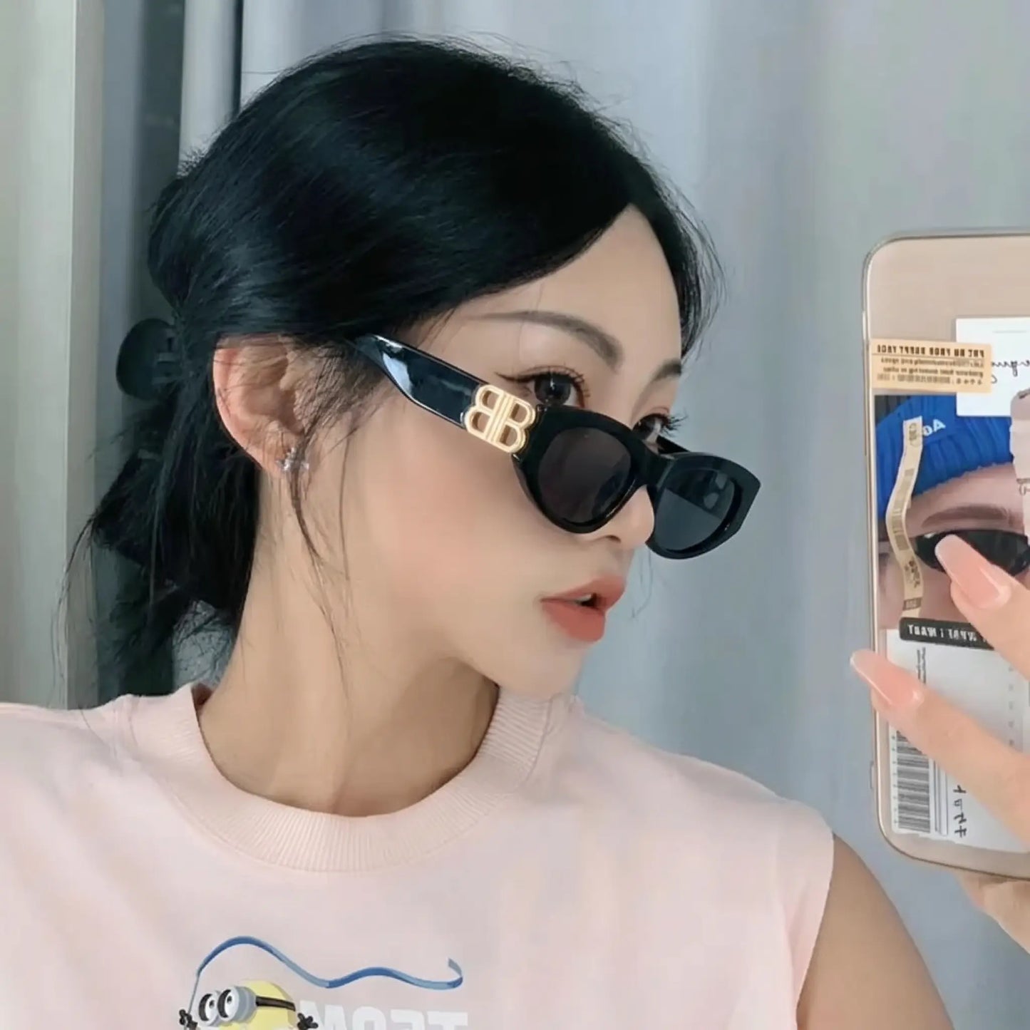 A woman wears glossy black cat-eye sunglasses with gold interlocking BB logo hardware and dark grey lenses, viewed from the side.