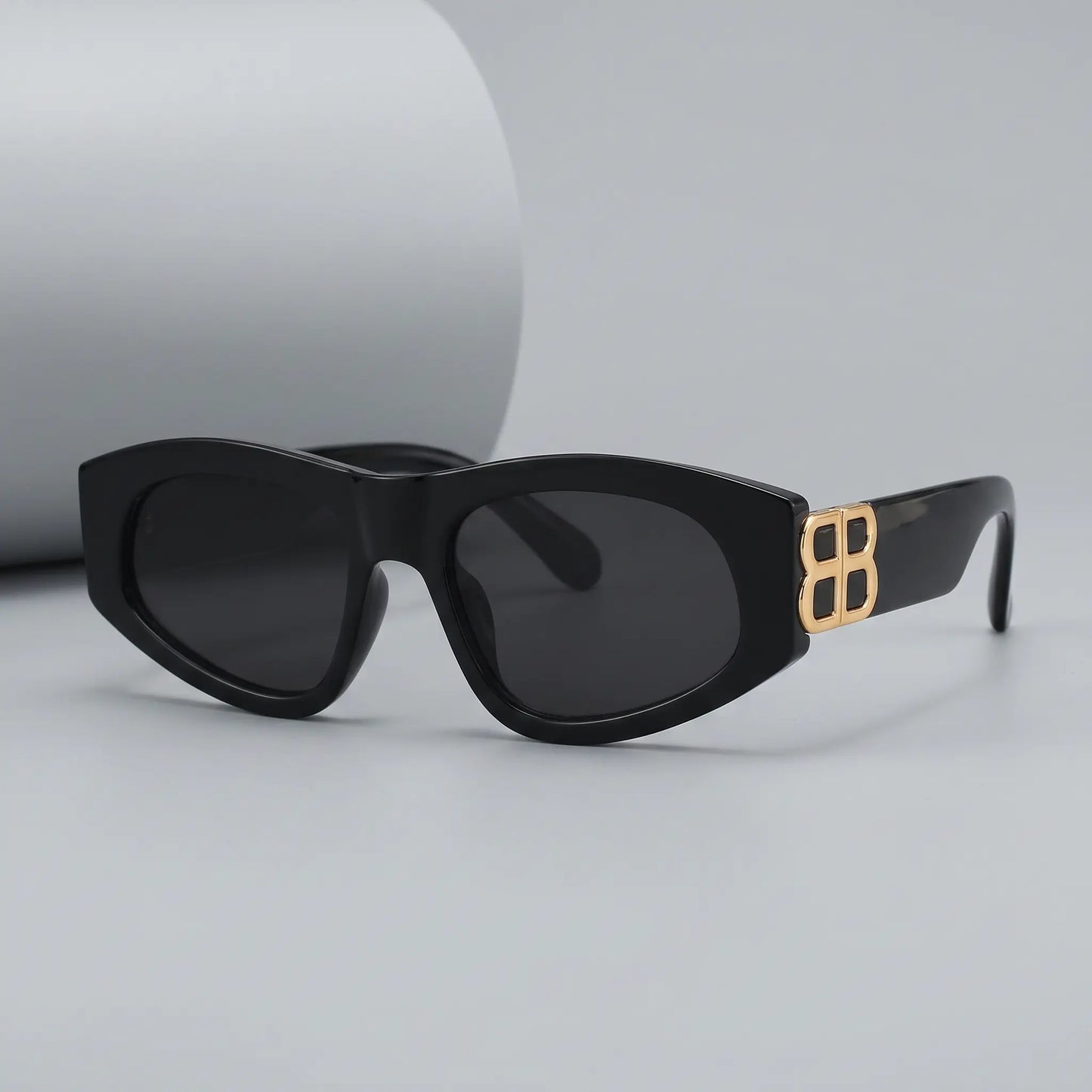 Zylos designer black cat-eye sunglasses with gold interlocking BB logo hardware and dark grey lenses, shown from a three-quarter front view.