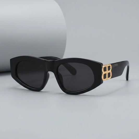 Zylos designer black cat-eye sunglasses with gold interlocking BB logo hardware and dark grey lenses, shown from a three-quarter front view.