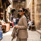 A woman wearing Zylos black cat-eye sunglasses with gold interlocking BB logo hardware while strolling through a vibrant market street, dressed in a chic beige linen suit.