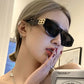 Close-up of a woman wearing glossy black cat-eye sunglasses featuring prominent gold-tone interlocking BB logo hardware on the temples and dark grey lenses.