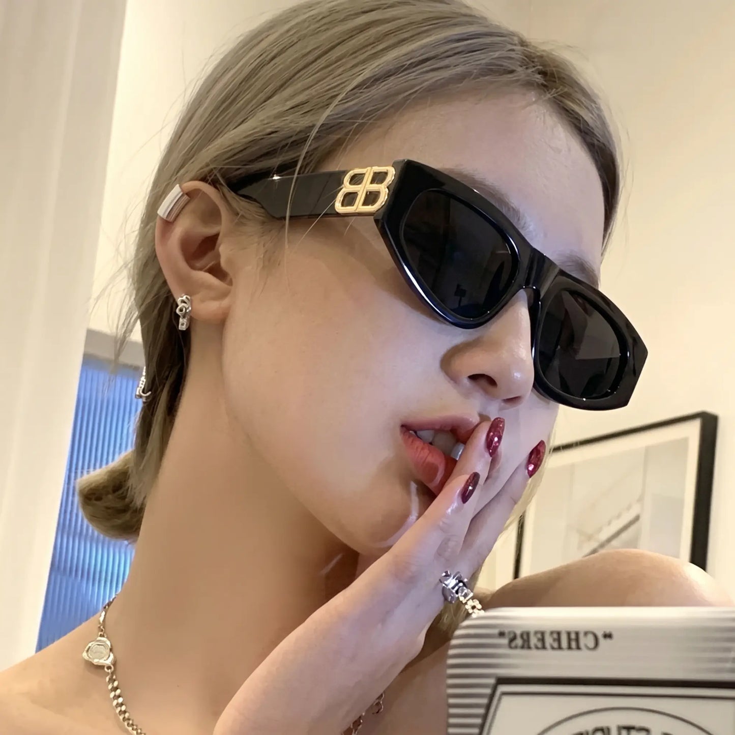 Close-up of a woman wearing glossy black cat-eye sunglasses featuring prominent gold-tone interlocking BB logo hardware on the temples and dark grey lenses.