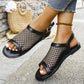 Elegant black mesh sandals with faux leather trim and adjustable buckle strap, shown on feet in a lifestyle outdoor setting with a straw bag in the background.