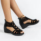 Black Zylos rhinestone wedge sandals with Roman-style straps, open toe, and gold-tone ankle chain, displayed on a model's feet against a white background.