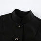 Close-up of a black Zylos sleeveless vest, showcasing its structured mandarin collar and polished gold-tone button front detailing. Features a matte woven fabric texture.