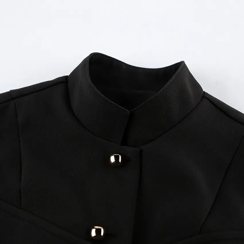 Close-up of a black Zylos sleeveless vest, showcasing its structured mandarin collar and polished gold-tone button front detailing. Features a matte woven fabric texture.