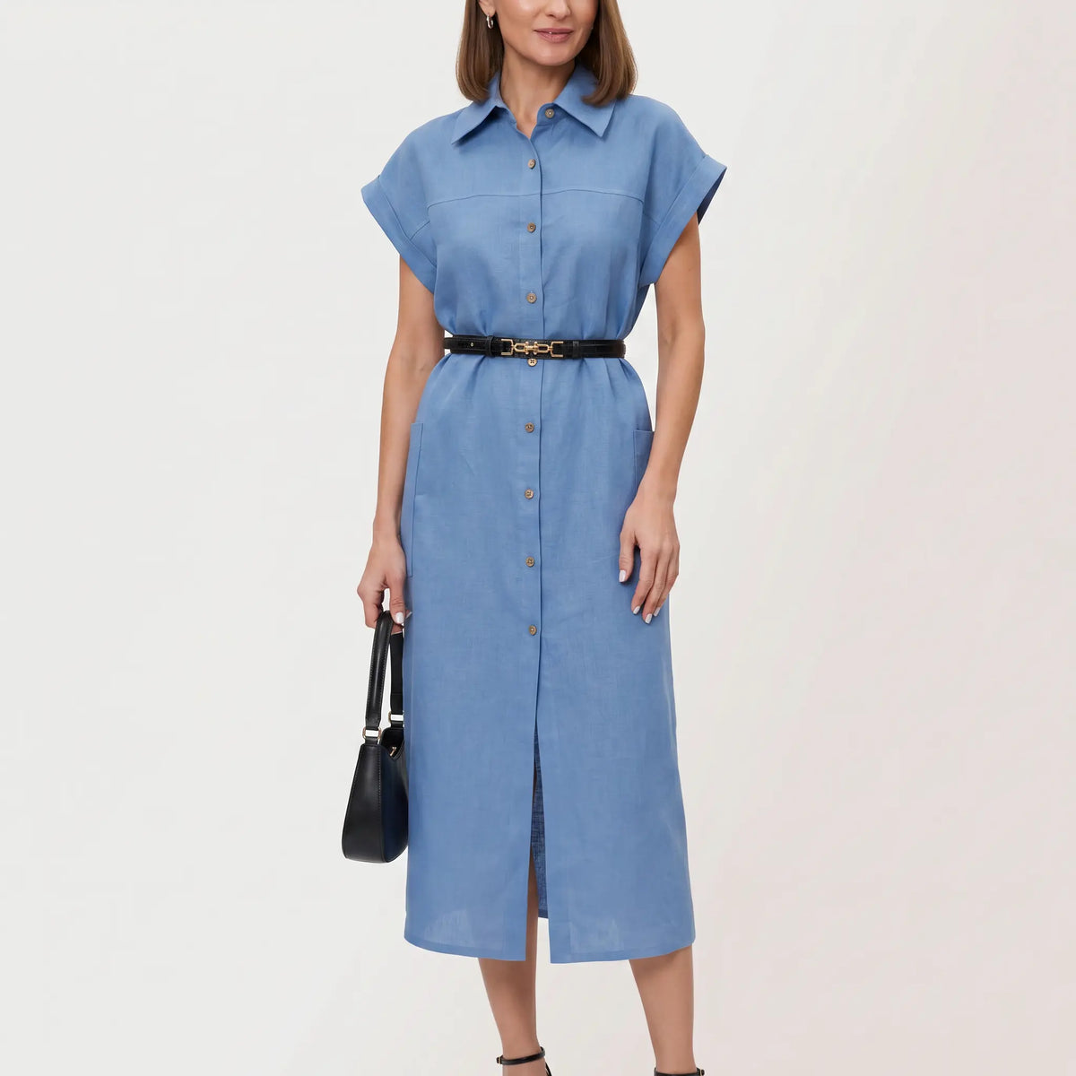 A woman models a sky blue linen blend midi shirt dress, featuring a turn-down collar, button-down front, cap sleeves, and a belted waist, shown in a studio setting. The dress has a high side slit.