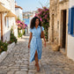A woman walks down a sunlit cobblestone street in a sky blue belted midi shirt dress with cap sleeves and a high side slit, embodying Mediterranean summer style.