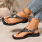 Bohemian black snake print flat sandals with a square toe and adjustable ankle strap, styled with distressed denim jeans on a model's feet.
