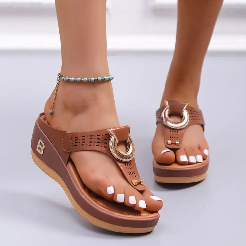 Women's brown Zylos wedge thong sandals with gold ring hardware and perforated straps, shown on feet with white toenails and a turquoise anklet.