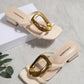 Pair of creamy ivory Zylos square toe slide sandals featuring large gold oval buckles and block heels, displayed in a flat-lay arrangement with subtle branding on the footbed.