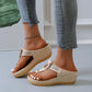 Creamy off-white Zylos women's wedge thong sandals with gold ring hardware and perforated strap detail, shown on a model's feet with light wash jeans and an ankle bracelet.
