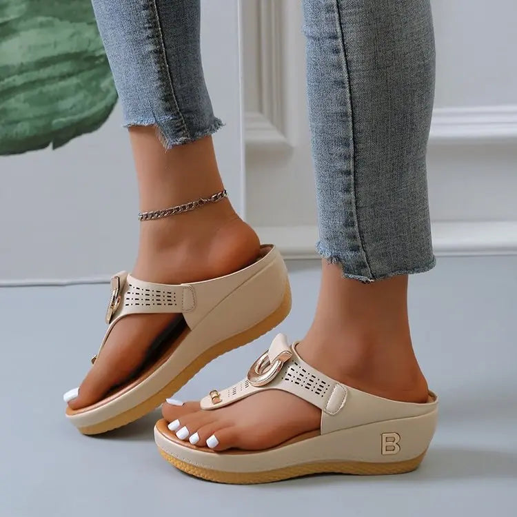 Creamy off-white Zylos women's wedge thong sandals with gold ring hardware and perforated strap detail, shown on a model's feet with light wash jeans and an ankle bracelet.