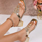 Close-up of Zylos metallic gold embellished thong sandals with crystal floral details, shown on a woman's feet with a chunky block heel and square toe.