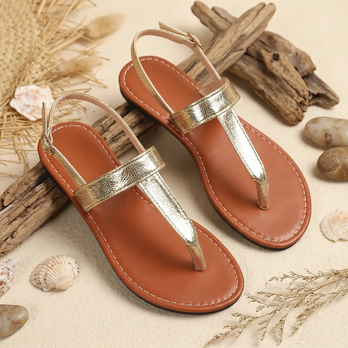 Gold metallic textured t-strap flat sandals with an adjustable ankle buckle and a tan footbed with white contrast stitching, styled flat lay.