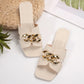 A pair of ivory Zylos flat slide sandals featuring a square toe and a wide strap adorned with a chunky gold-tone chain, presented on a studio background with subtle styling elements.