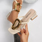Creamy ivory Zylos square toe slide sandals featuring a large oval gold buckle and a comfortable block heel, shown on a model's feet.