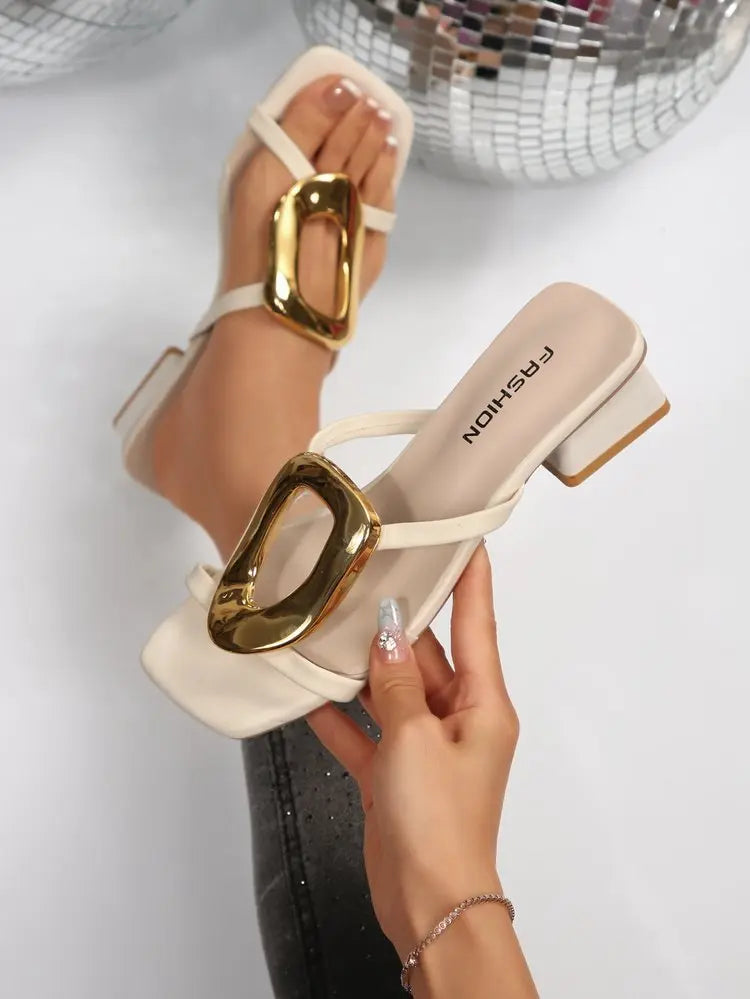 Creamy ivory Zylos square toe slide sandals featuring a large oval gold buckle and a comfortable block heel, shown on a model's feet.