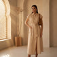 Elegant beige linen blend shirt dress with cap sleeves and a tie-waist, shown on a model in a sunlit interior setting with architectural details.