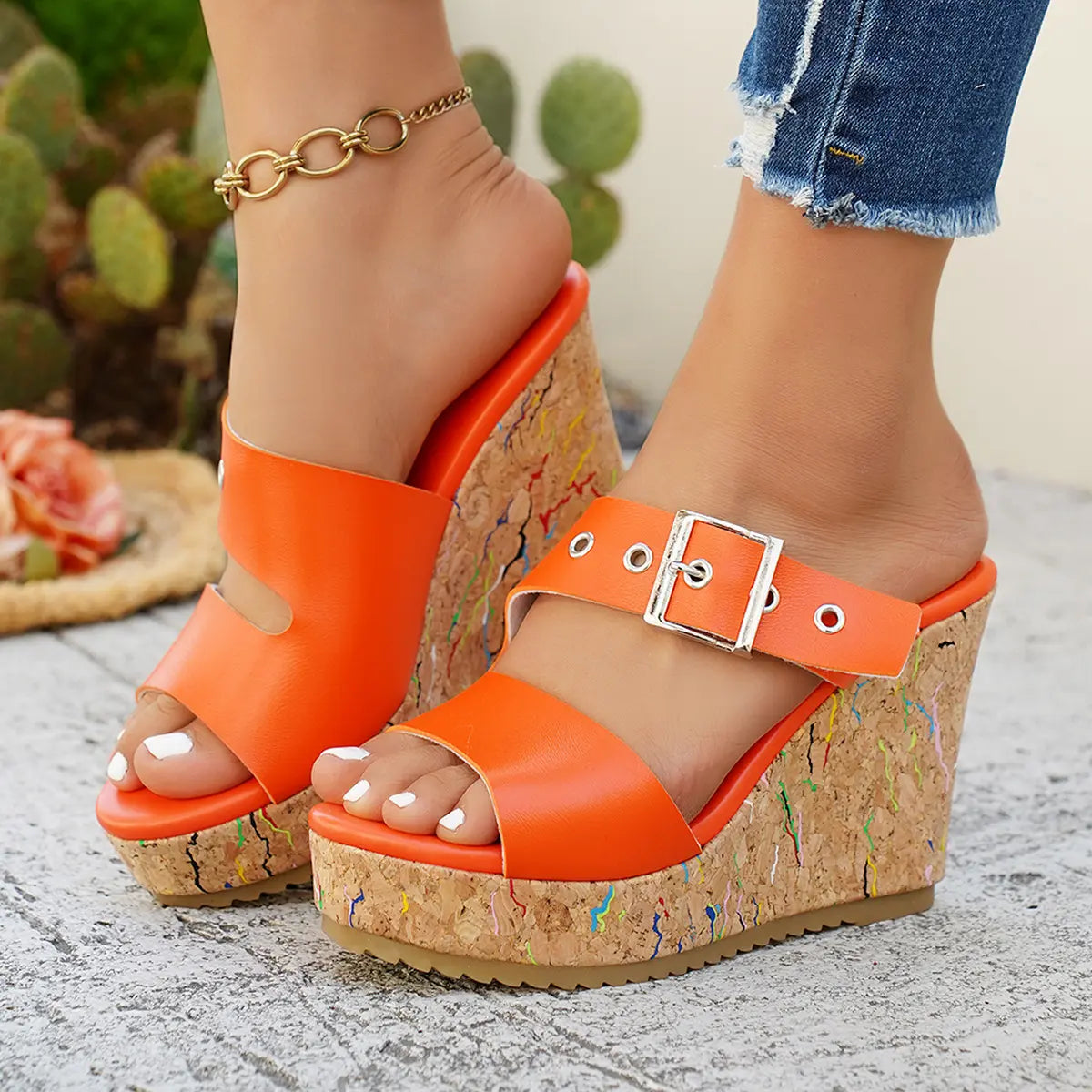 Zylos vibrant orange peep-toe wedge sandals on a model's feet, featuring a cork-effect heel with colorful flecks and an adjustable silver buckle strap, styled with distressed denim.