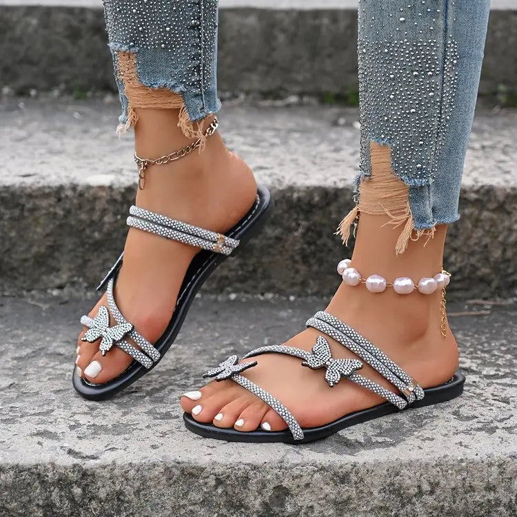 Lifestyle view of Zylos women's rhinestone butterfly flat sandals worn with distressed denim jeans, showcasing sparkling butterfly embellishments and delicate straps.