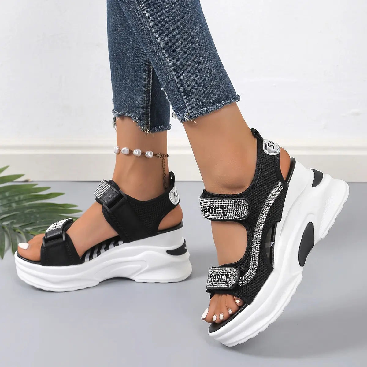 Model wearing black Zylos sporty chic platform sandals with rhinestone-embellished straps and a chunky white sole, styled with denim jeans and a pearl anklet.