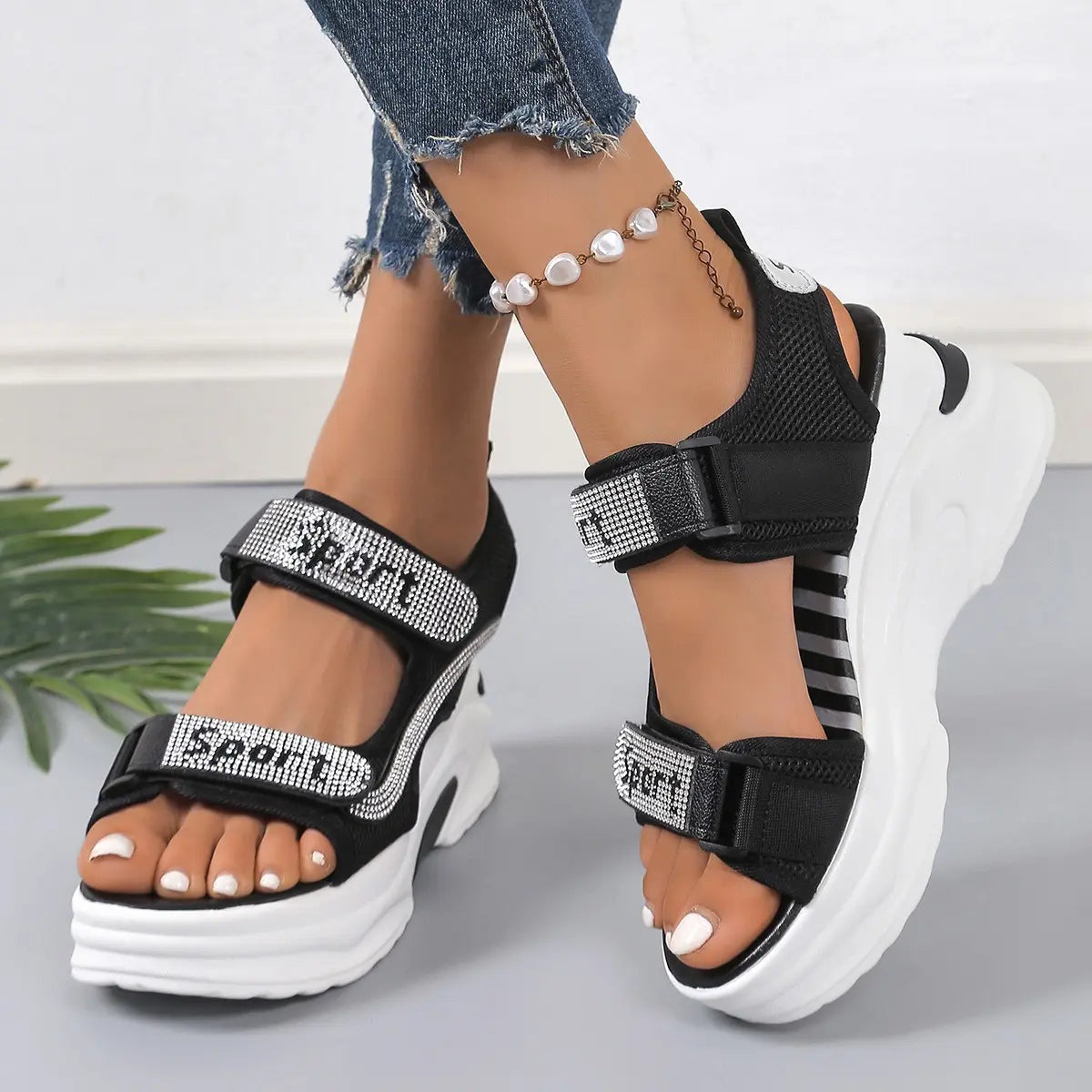 Zylos Sporty Chic platform sandals in black, featuring dazzling rhinestone-embellished mesh straps with hook-and-loop closures and a chunky white EVA sole, worn on feet with ripped denim jeans.
