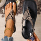 Close-up of a woman's foot wearing a Zylos bohemian flat sandal with black and beige snake print, featuring a square toe and adjustable ankle strap, styled with distressed denim and a gold anklet.