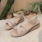Warm beige Zylos casual summer wedge sandals with adjustable hook-and-loop straps and decorative perforations, shown on a sandy beach setting with plants.
