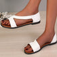 Close-up of white Zylos flat Roman sandals worn on a model's feet, showcasing the geometric faux leather straps, delicate ankle strap, and studded sole edge on a subtly textured background.
