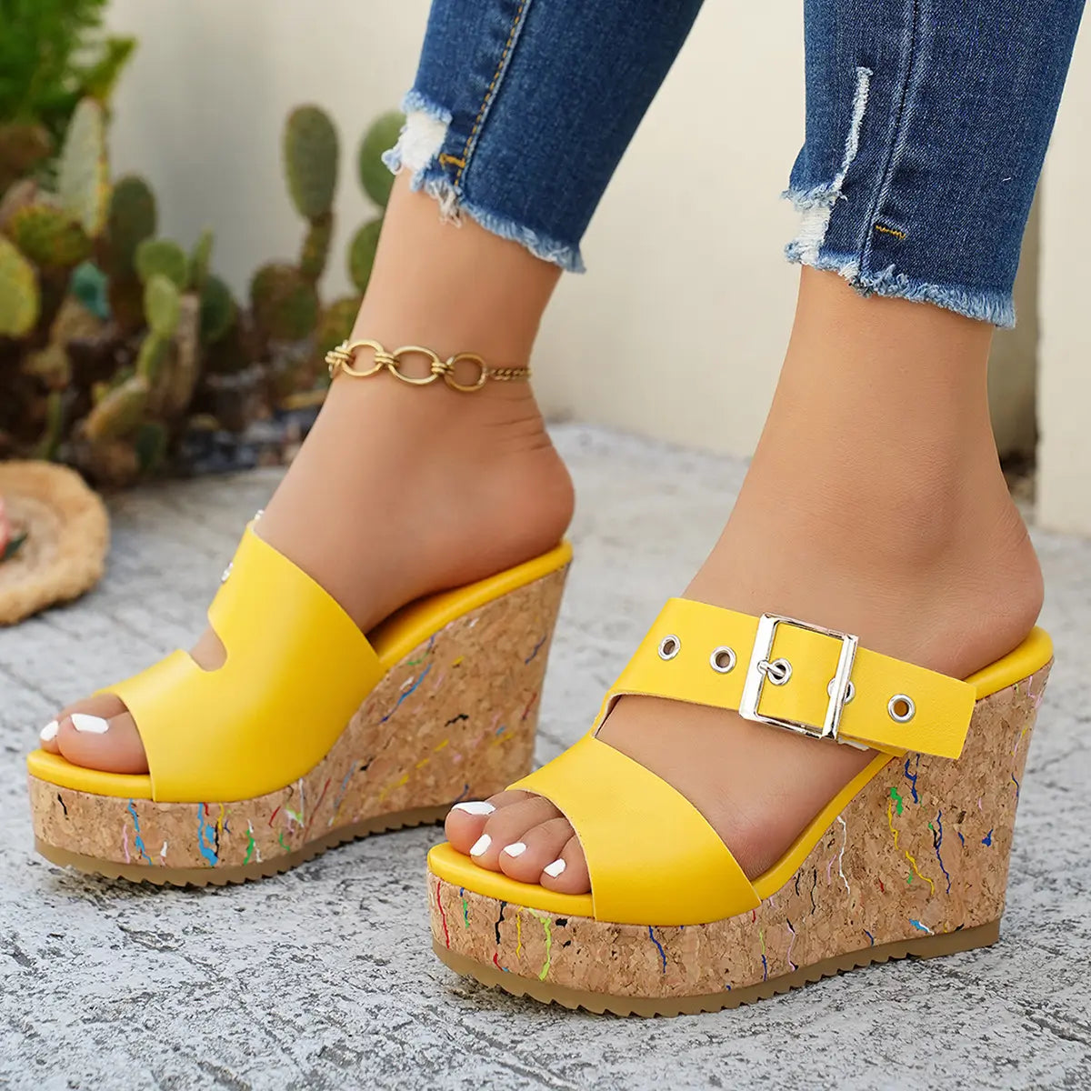 Yellow Zylos women's wedge sandals featuring a peep-toe design, adjustable silver buckle strap, and a unique cork-effect wedge with colorful flecks. Styled with distressed denim jeans in an outdoor setting.