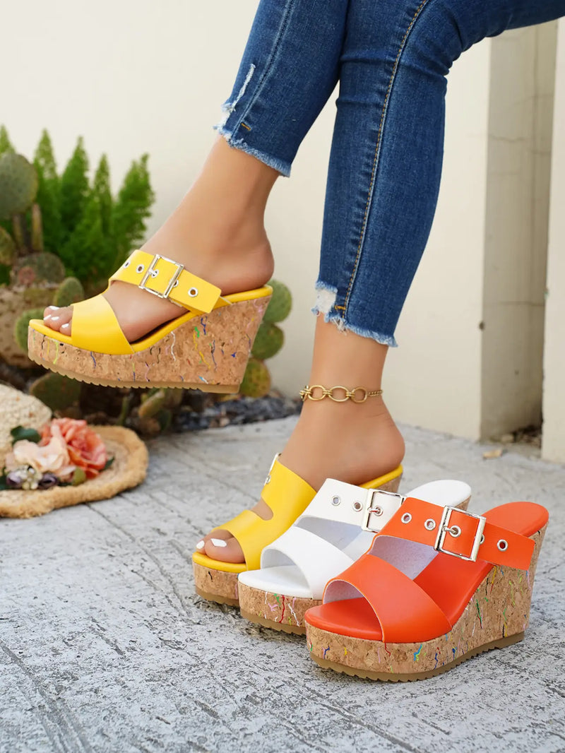 A woman's legs wearing yellow Zylos peep-toe wedge sandals with a multi-colored flecked cork wedge and silver buckle strap, styled with distressed denim jeans, alongside white and orange variants.