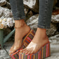 Bohemian-inspired platform wedge sandals with vibrant multi-colored stripes and a clear PVC strap, worn by a woman in jeans.