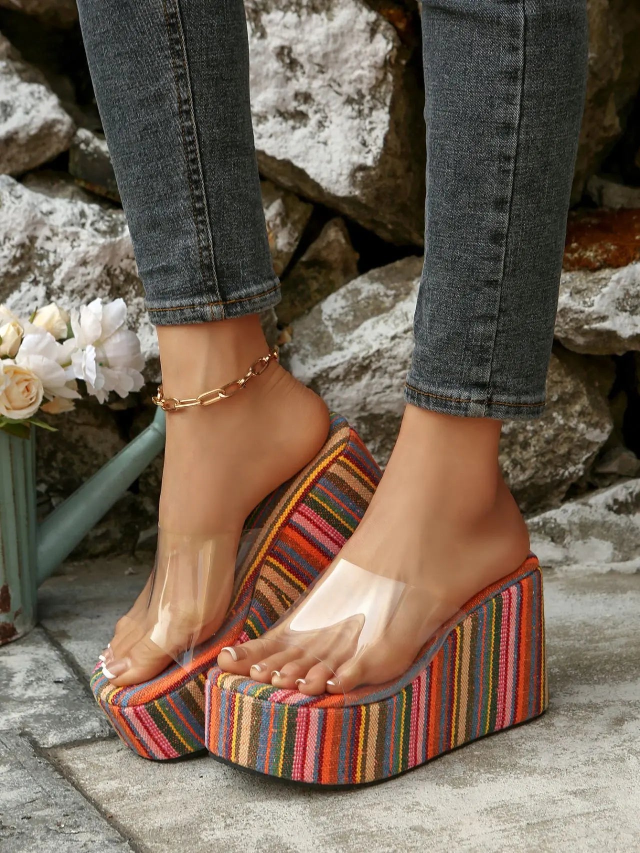 Bohemian-inspired platform wedge sandals with vibrant multi-colored stripes and a clear PVC strap, worn by a woman in jeans.